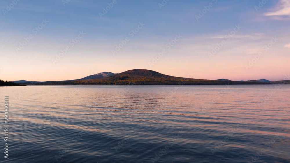 Zuratcul mountain lake in early morning with Nurgush and Lucash mounts on background; pink and purple colours of morning sunrise sun; national park, amazing autumn sky reflecting on water surface