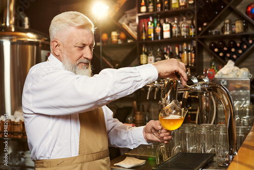 Barman pouring light beer in glass with beer tap.
