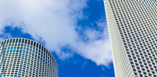 modern clean city urban view from below two gray exterior skyscraper buildings on blue sky white clouds background copy space 