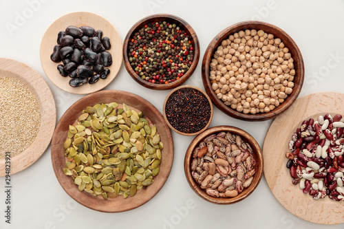 top view of wooden bowls with diverse beans, quinoa, peppercorns, pumpkin seeds and chickpea on white marble surface