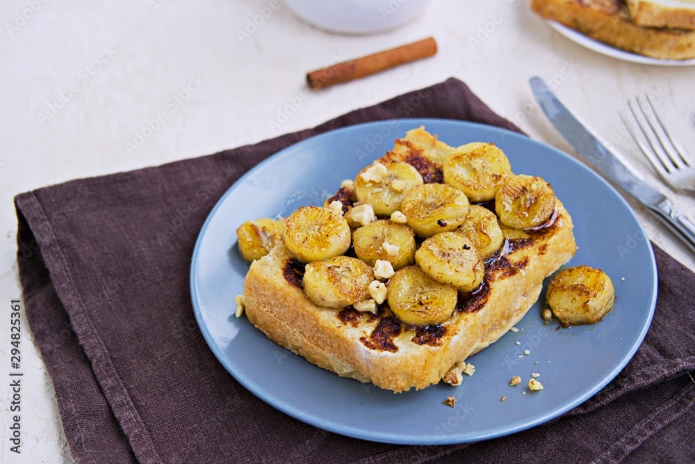 Breakfast, french toasts with banana, walnuts and honey on a gray plate on a light concrete background. French cuisine