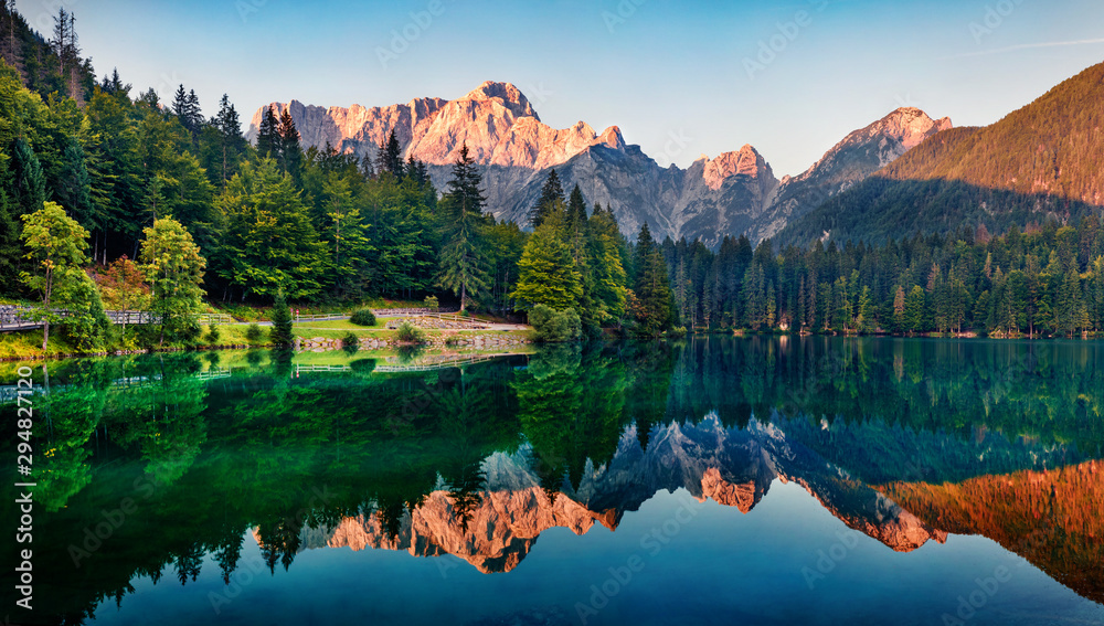 Calm morning view of Fusine lake. Colorful summer sunrise in Julian Alps with Mangart peak on background, Province of Udine, Italy, Europe. Beauty of nature concept background. - obrazy, fototapety, plakaty 