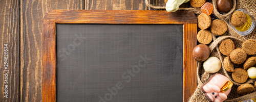Dutch holiday Sinterklaas background with black chalkboard, pepernoten, traditional sweets strooigoed and carrots for Santa's horse. Flat lay and copy space. Banner photo