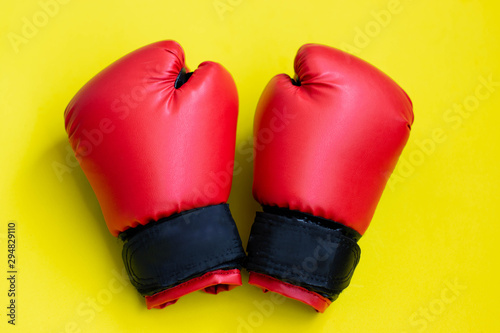 Red boxing gloves on a yellow background. © Elena
