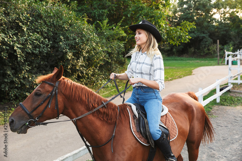 Smiling attractive young blonde girl riding a horse