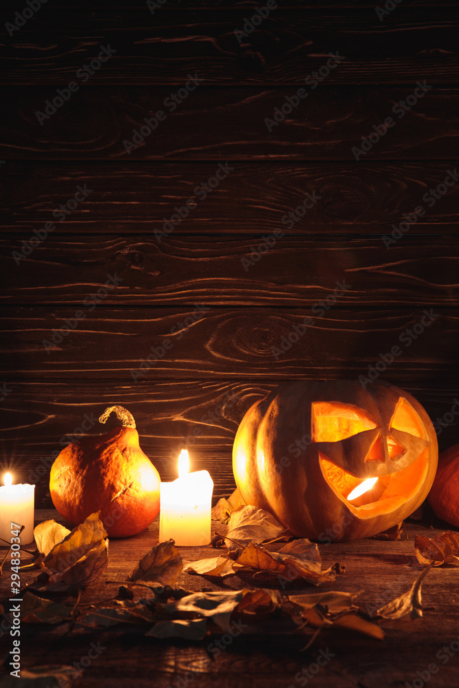 Fototapeta premium carved spooky Halloween pumpkin, autumnal leaves and burning candles on wooden rustic table