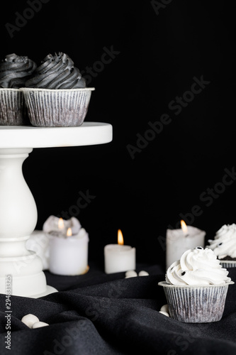 delicious Halloween cupcakes on stand near burning candles isolated on black