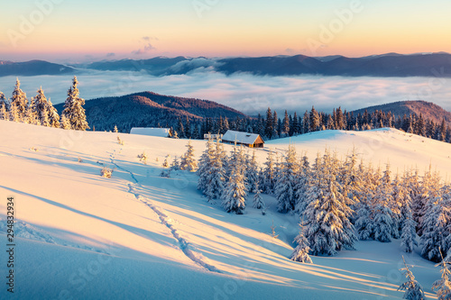 Abandoned mountain village in high mountains. Bright winter scene of Carpathians. Misty sunrise in mountain valley with snow covered fir trees. Beauty of nature concept background.