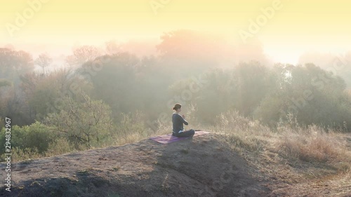 Aerial video. Young woman doing yoga in quiet scenery. Yoga girl practicing pilates on top of the hill. Yoga, sport and healthy lifestyle concept