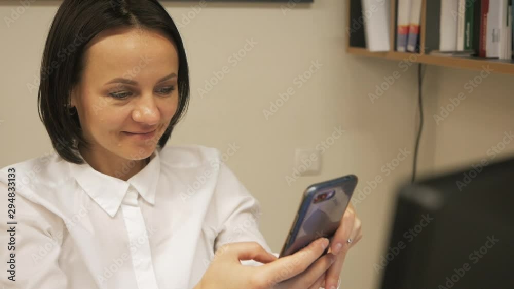 Cute brunette looks into the smartphone and smiles from what she saw Cute brunette looks into the smartphone and smiles from what she saw