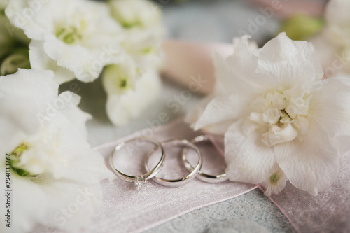 Modern wedding jewelry. Closeup of two wedding rings and engagement ring on natural background with flowers and leaves.