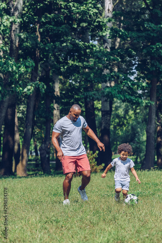happy african american father and son playing football in park