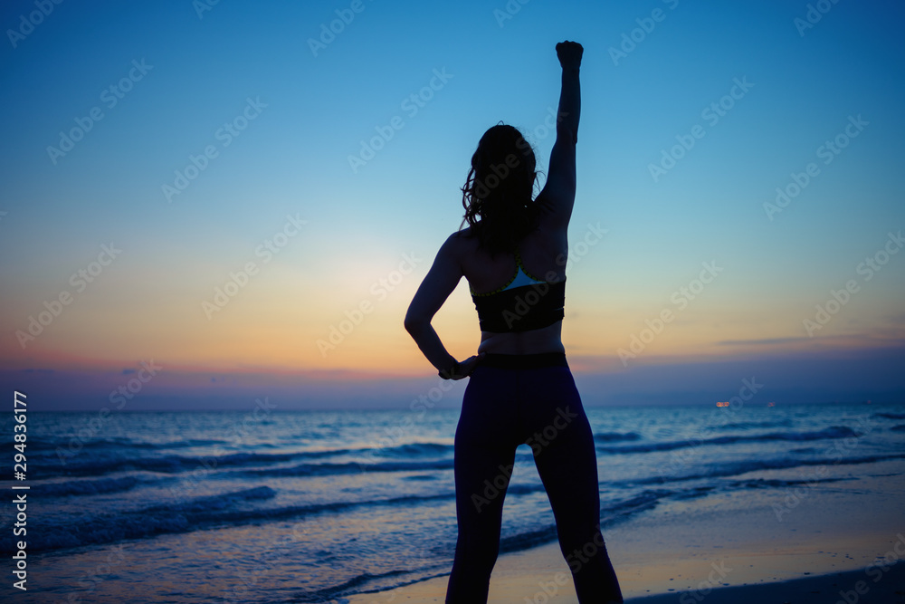 woman with raised arms rejoicing on ocean shore in evening