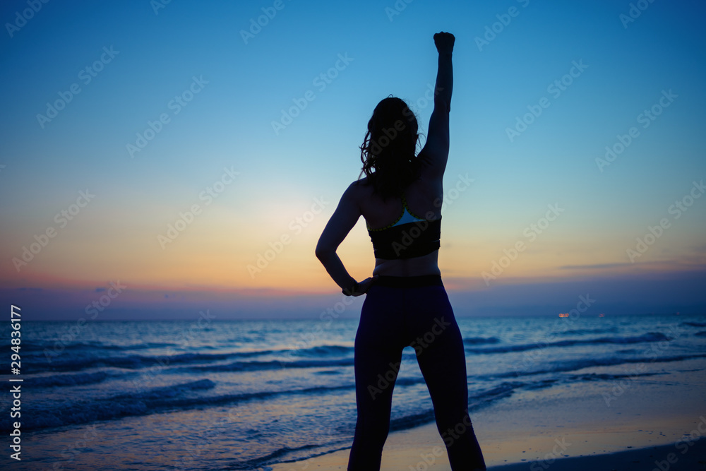 Fototapeta premium woman with raised arms rejoicing on ocean shore in evening