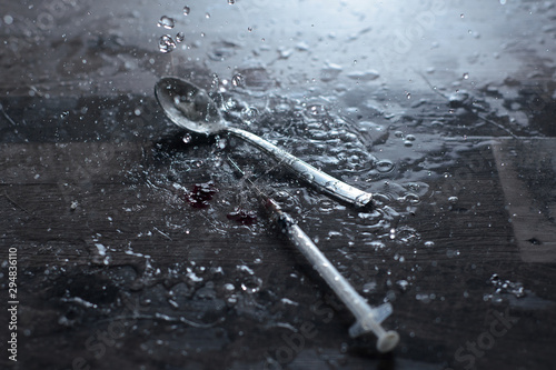 a teaspoon and a syringe with a drug in the rain on a gray surface, near a drop of blood © Анастасия Гайкова