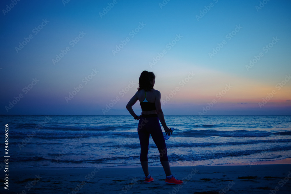 active sports woman with water relaxing on seacoast in evening