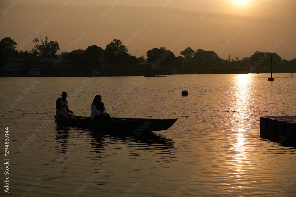 Silhouette of indonesian fisherman on wooden boat in the sunset at dock lake