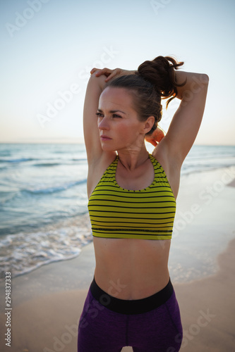 young sports woman on ocean coast in evening stretching