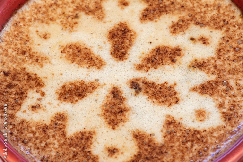 A foamy mug of cappuccino coffee with chocolate snowflake motif and a snowy background with a scattering of coffee beans sets the scene for a festive Christmas and warming up in cold winter weather