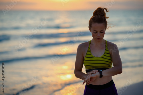 Fototapeta Naklejka Na Ścianę i Meble -  young sports woman on ocean shore at sunset using smart watch