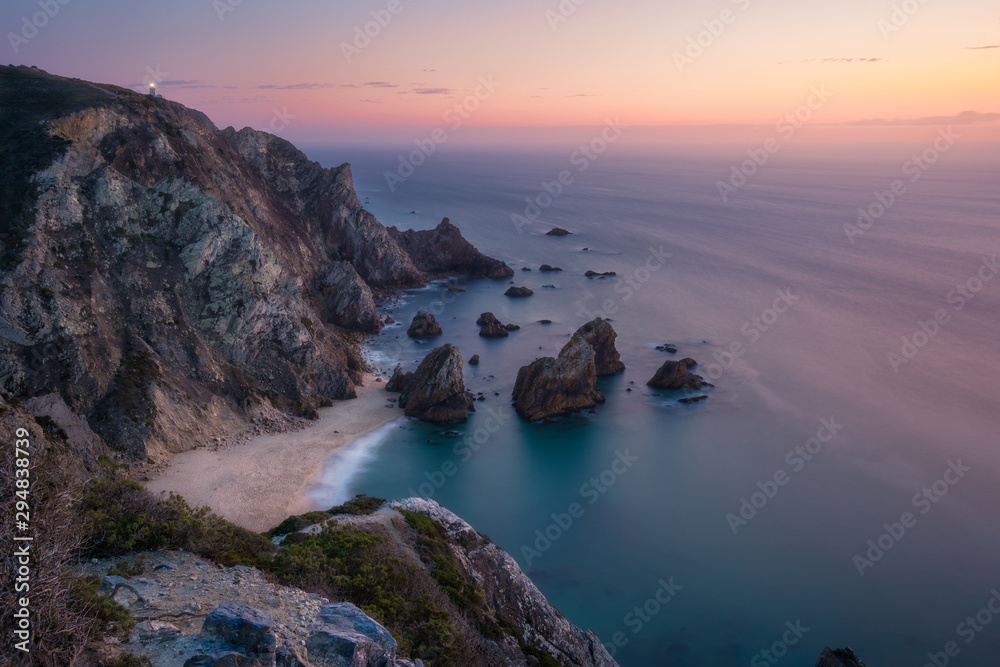 Sunset over a hidden surreal Praia Da Ursa Beach. Cabo Da Roca with light-house in background. Atlantic coast, Portugal, Europe Sunset over a hidden surreal Praia Da Ursa Beach. Cabo Da Roca with light-house in background. Atlantic coast, Portugal, Europe