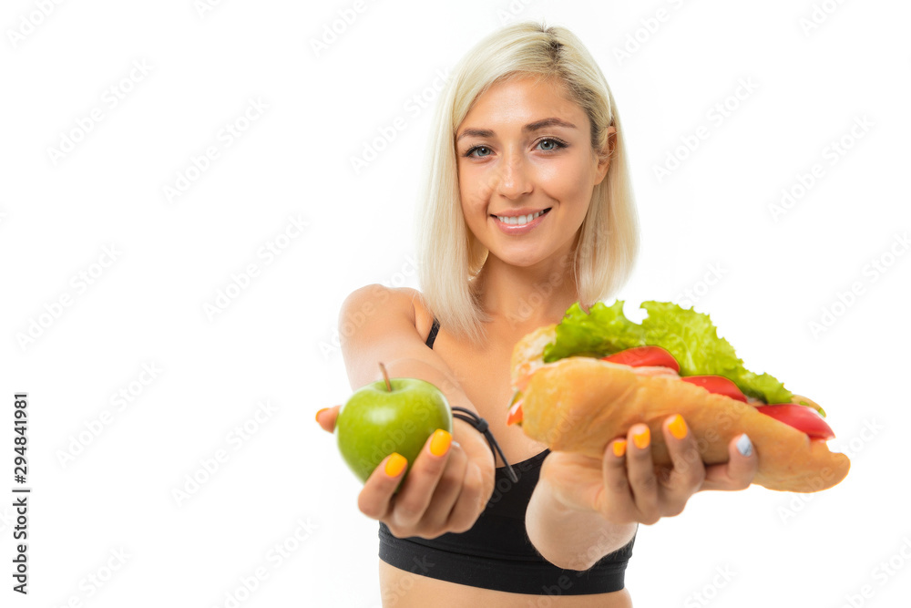 A young sports girl with blonde hair in a black sports top and black leggings holds a green apple and sandwich. A young sports girl with blonde hair in a black sports top and black leggings holds a green apple and sandwich.