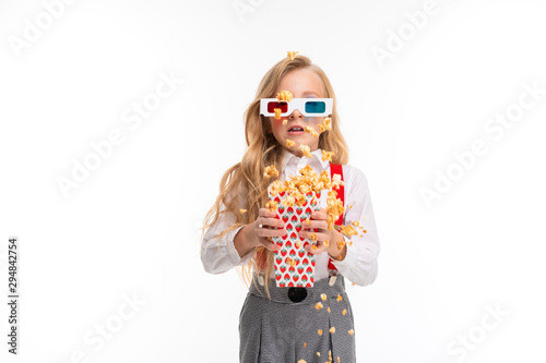 A little girl with long blonde hair in her glasses 3-D eat popcorn.