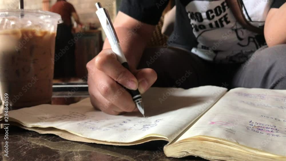 Close up a student writing on a notebook in coffee shop.