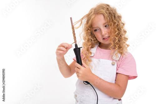 A little girl with red heap hair in a jersey, white jumpsuit, white sneakers spins her hair on a thin plow.