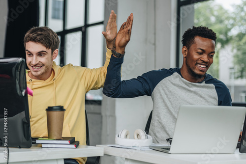 happy multicultural programmers giving high five while working in office together photo