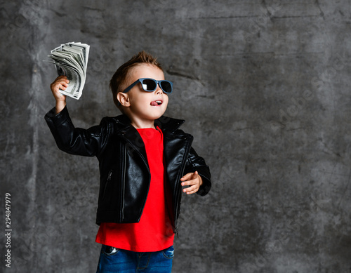 Looking up rich kid boy in sunglasses, leather jacket and red t-shirt holding a bundle of dollars going to throw it up
