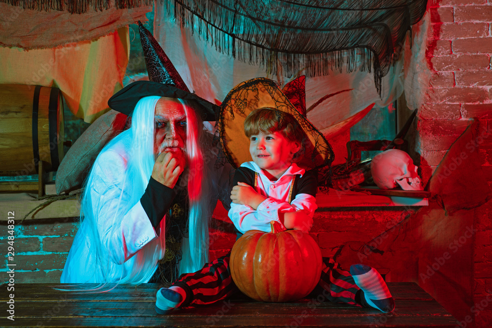 Cheerful children in Halloween costumes and senior Devil with Witch hat posing with pumpkin over Halloween background. Happy Father and Children boy in Halloween Costume.