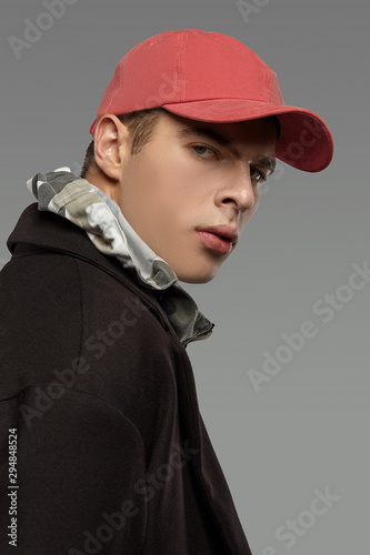 Close-up portrait shot of a short-haired European man dressed in a dazzle hooded top, a black jacket and a poppy-red cotton baseball cap.  photo