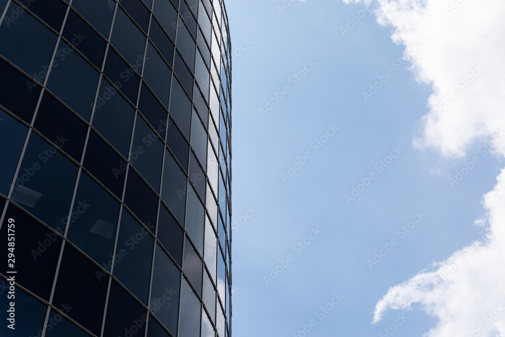 Side view of dark glass facade building in business city area with sky and clouds on background. Side view of dark glass facade building in business city area with sky and clouds on background.