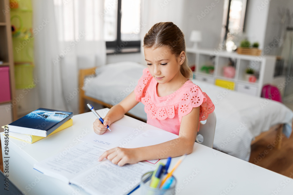 children, education and learning concept - student girl with book writing to notebook at home