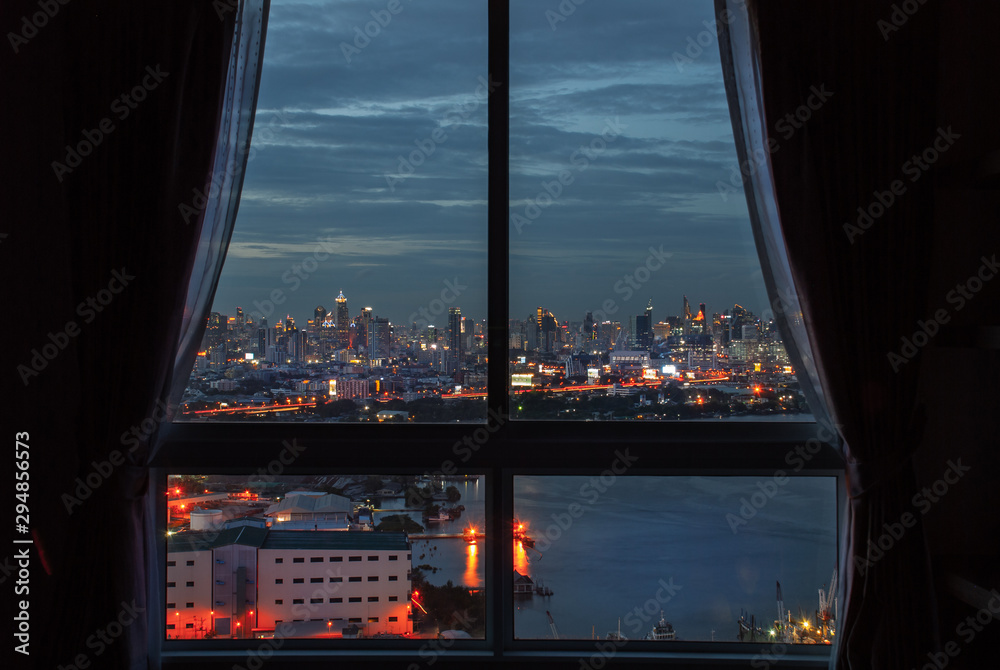 The beautiful view of Bangkok, the beautiful skyscrapers along the Chao Phraya River during sunset seen through a bedroom window.