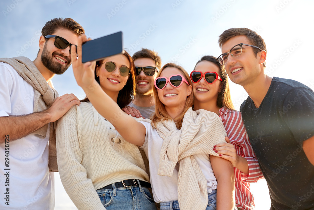friendship, leisure and people concept - group of happy friends taking selfie by smartphone in summer