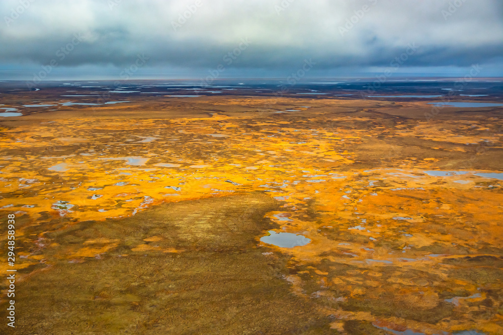 Photographing from a helicopter in the Arctic. Autumn nature landscape of the northern tundra. The landscape of many lakes, rivers, variegated mosses and lichens. Gloomy autumn sky.