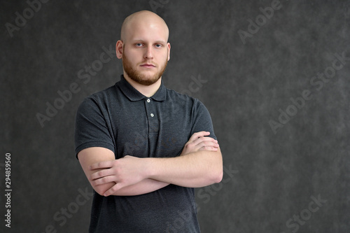 Fototapeta Portrait of a handsome bald man in a gray t-shirt on a gray background in the studio