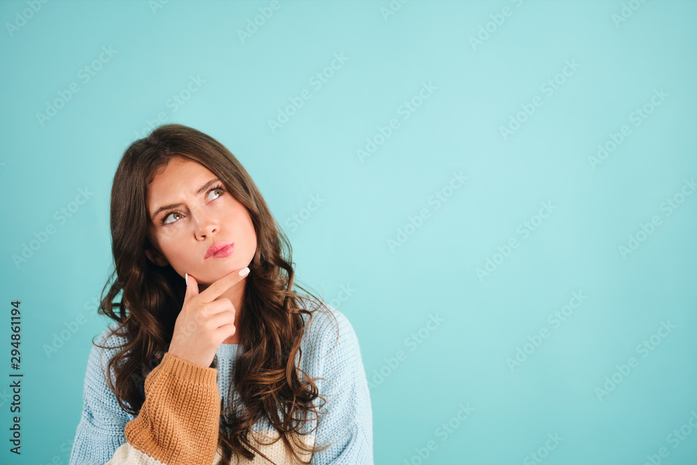 Fototapeta premium Attractive thoughtful girl in sweater dreaming over blue background