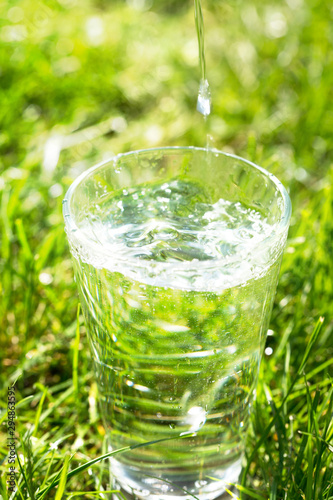 A glass of clean transparent drinking water on a grass background.