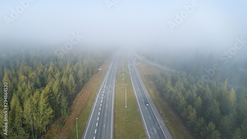 Cars drivinig on a country highway passing through the forest.  Rural landscape in foggy day.