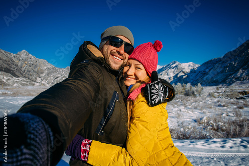 Handsome happy couple taking selfie against snow-capped mountain and blue sky. New year vacations, great weather for winter activities.
