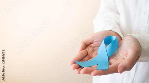 Men's health and Prostate cancer awareness campaign in November month. Close up of young man hands holding light blue ribbon awareness. Symbol for support men who living w/ cancer. Copy space.