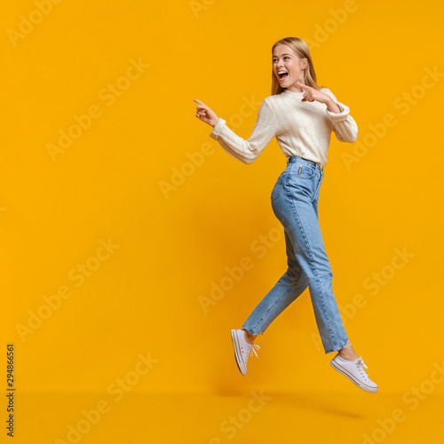 Young girl jumping in air and pointing on copy space
