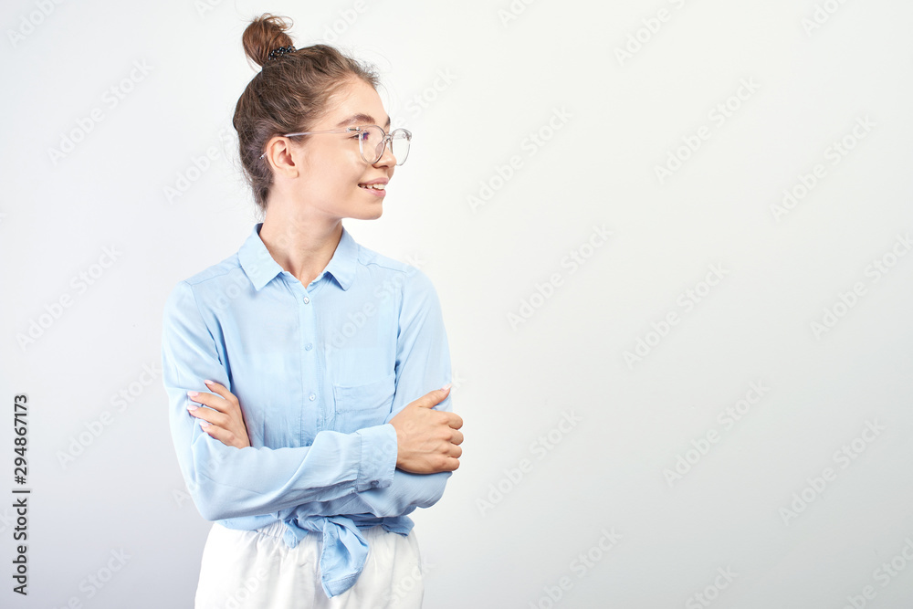 Portrait of Asian Kazakh student girl with bun of hair on head and glasses with arms crossed smiling and looking to the side with copy space on white background Portrait of Asian Kazakh student girl with bun of hair on head and glasses with arms crossed smiling and looking to the side with copy space on white background