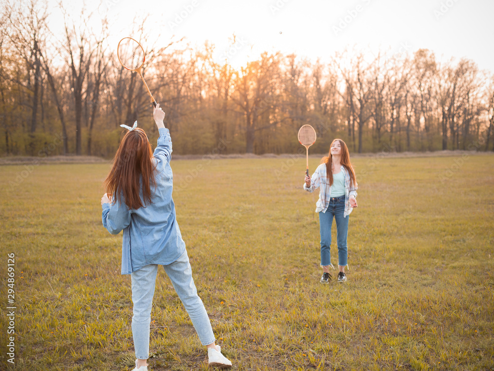 Fototapeta premium Two girls play badminton on the field at sunset. Best friends