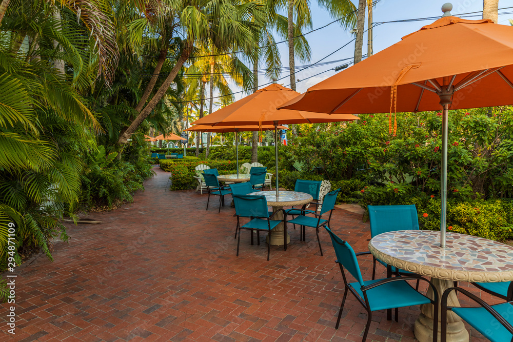 Beautiful view of outdoor tables. Blue chairs and orange umbrellas on green palm trees and blue sky background. Key West, Florida. USA. 