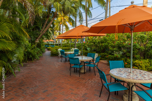 Beautiful view of outdoor tables. Blue chairs and orange umbrellas on green palm trees and blue sky background. Key West, Florida. USA. 
