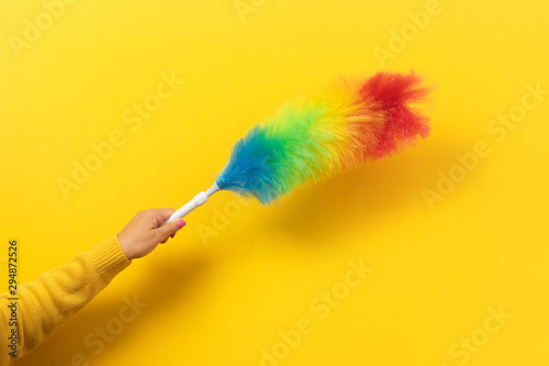 Colorful feather duster in hand on yellow background. Cleaning concept. photo